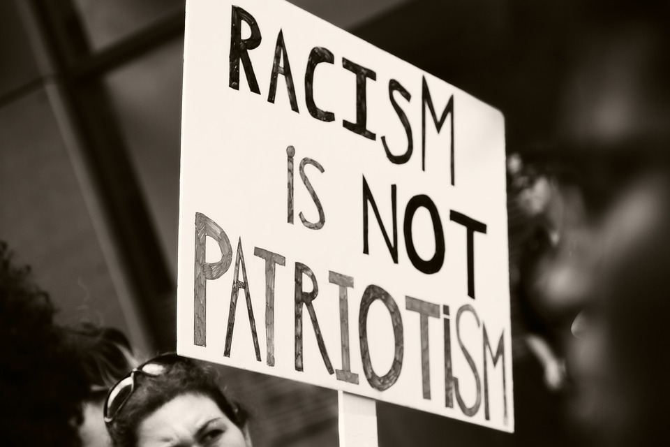 Woman holding a protest sign reading "racism is not patriotism"